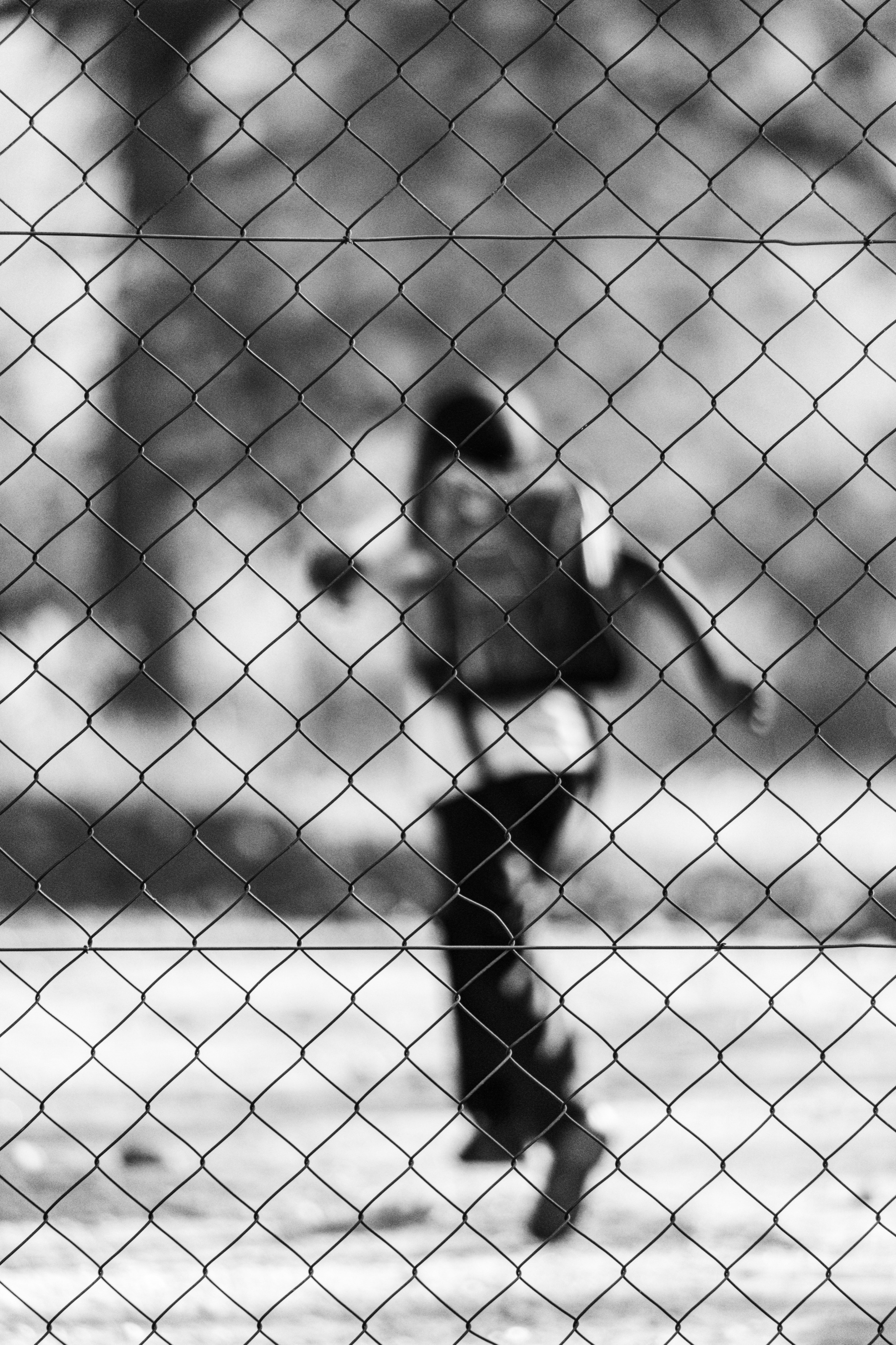 A figure running behind a wire fence, out of focus, in black and white.