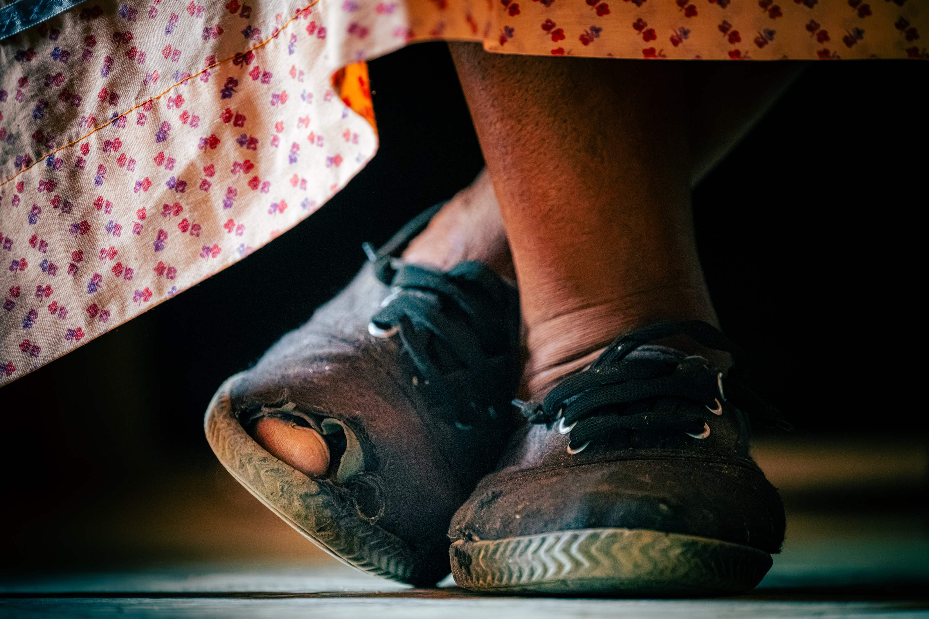 A person's feet in worn sneakers and a flowered skirt, shot from ground level.