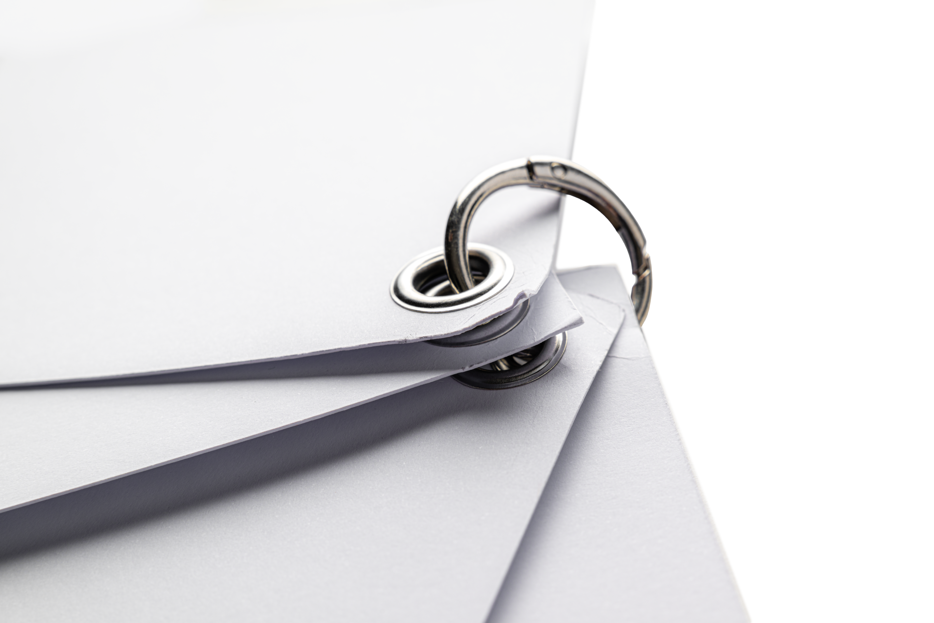 A close-up of a metal ring holding together a few eyeleted white cards.